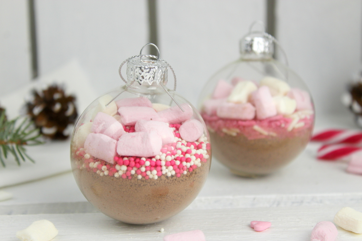 Trinkschokolade mit bunten Streuseln, Zuckerstange und Marshmallows in einer Christbaumkugel