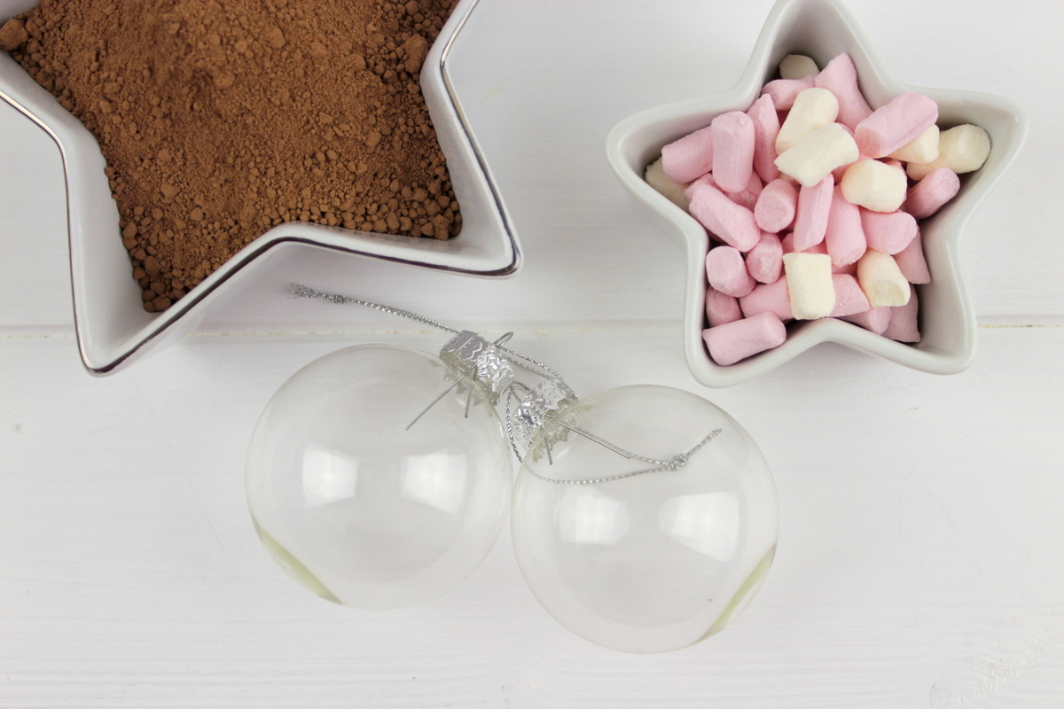 Trinkschokolade mit bunten Streuseln, Zuckerstange und Marshmallows in einer Christbaumkugel