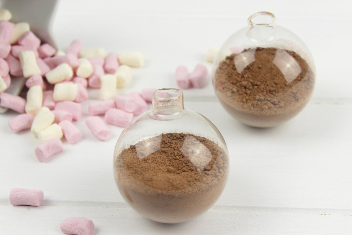 Trinkschokolade mit bunten Streuseln, Zuckerstange und Marshmallows in einer Christbaumkugel