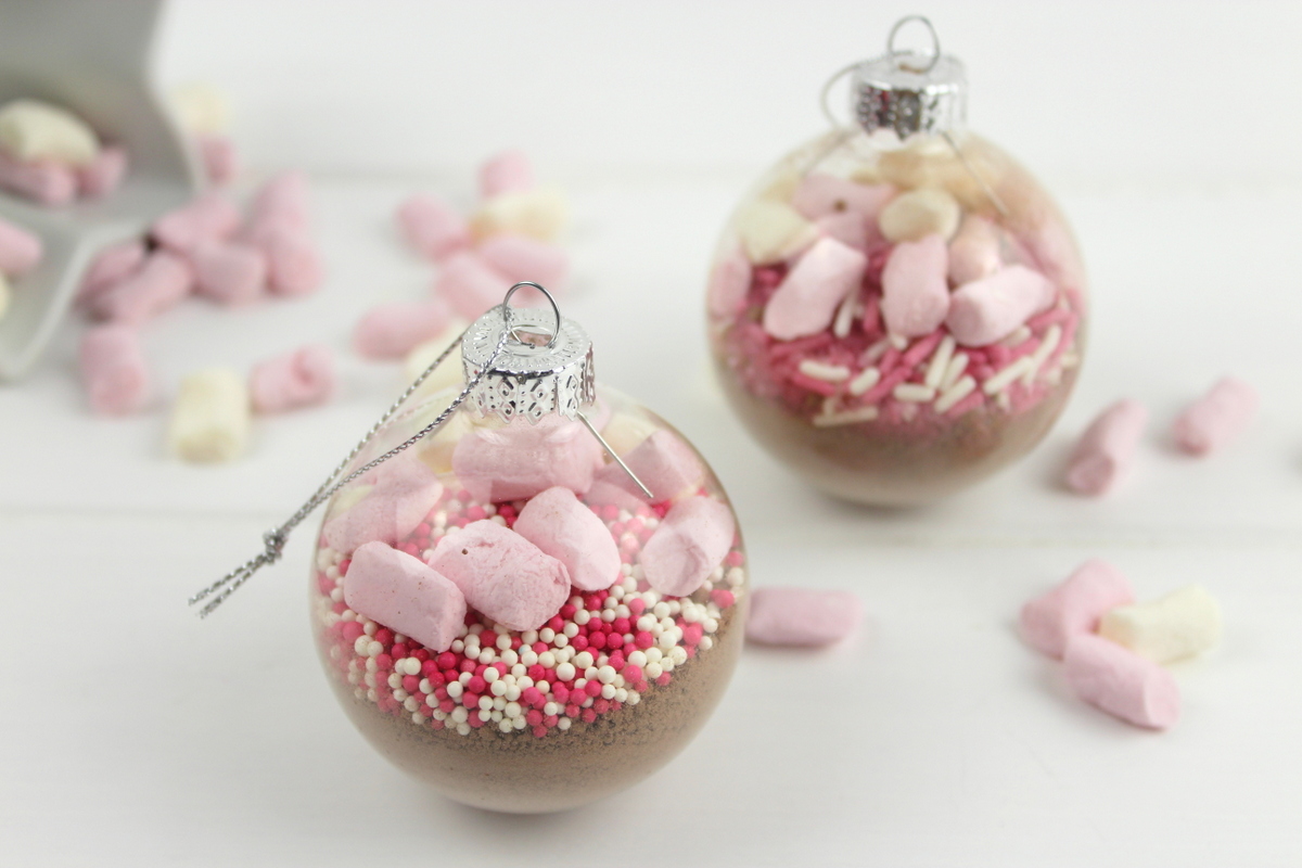 Trinkschokolade mit bunten Streuseln, Zuckerstange und Marshmallows in einer Christbaumkugel