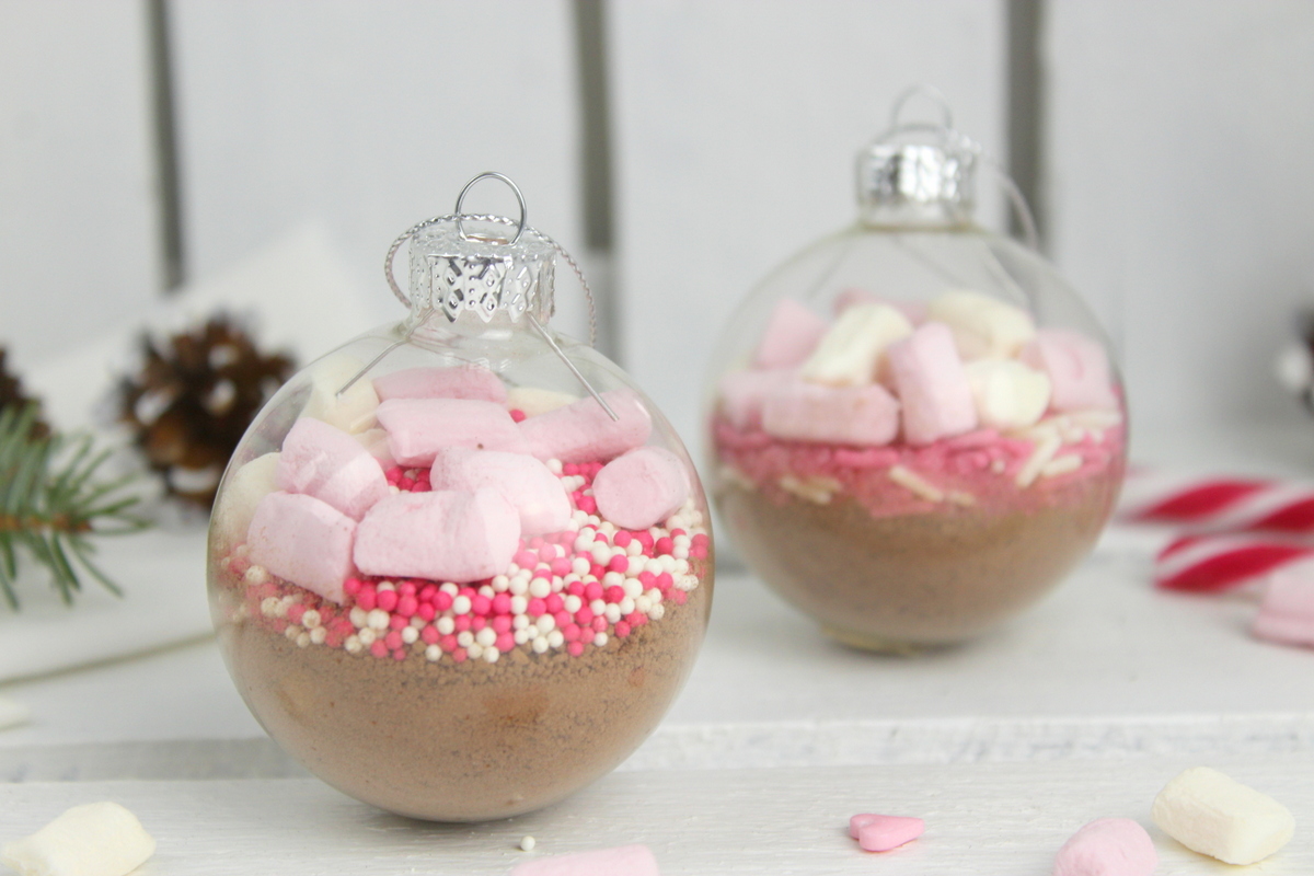 Trinkschokolade mit bunten Streuseln, Zuckerstange und Marshmallows in einer Christbaumkugel