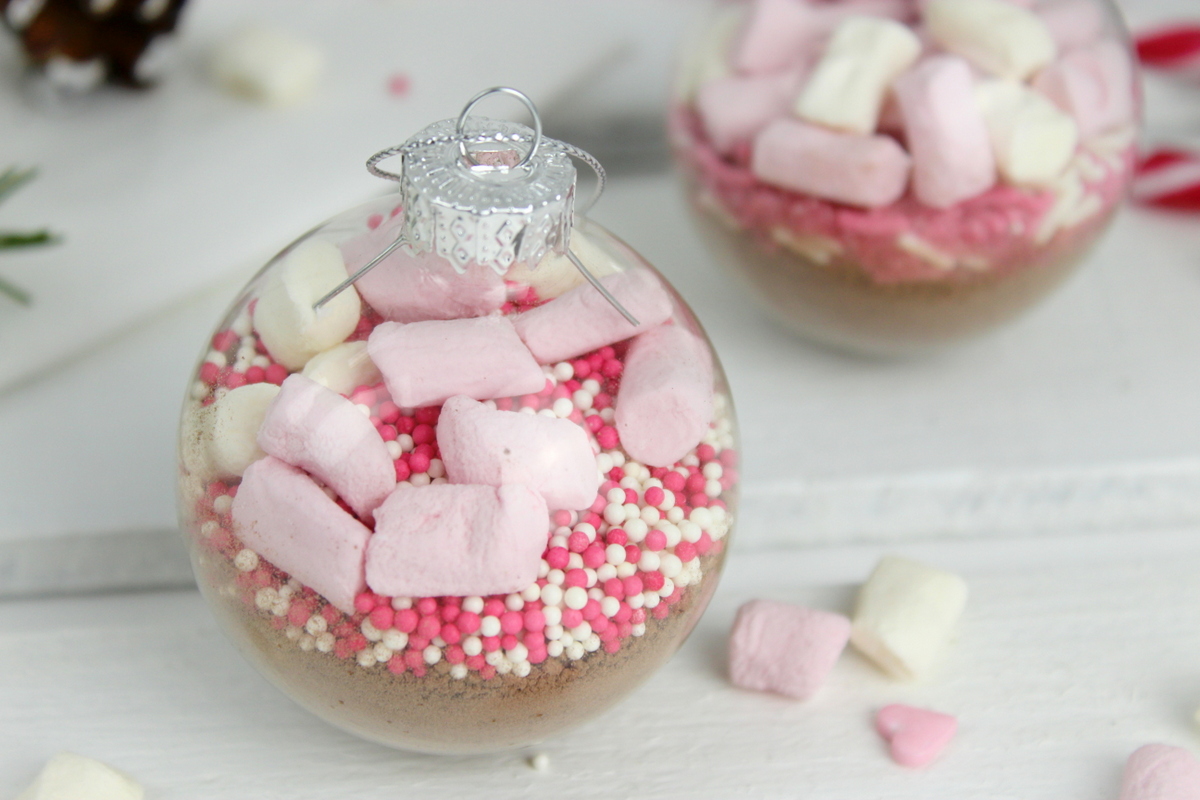 Trinkschokolade mit bunten Streuseln, Zuckerstange und Marshmallows in einer Christbaumkugel