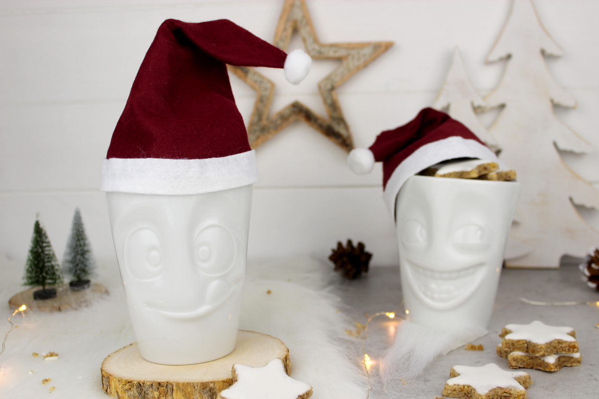 lustige Tassen mit Weihnachtsmannmützen gefüllt mit Zimtsternen