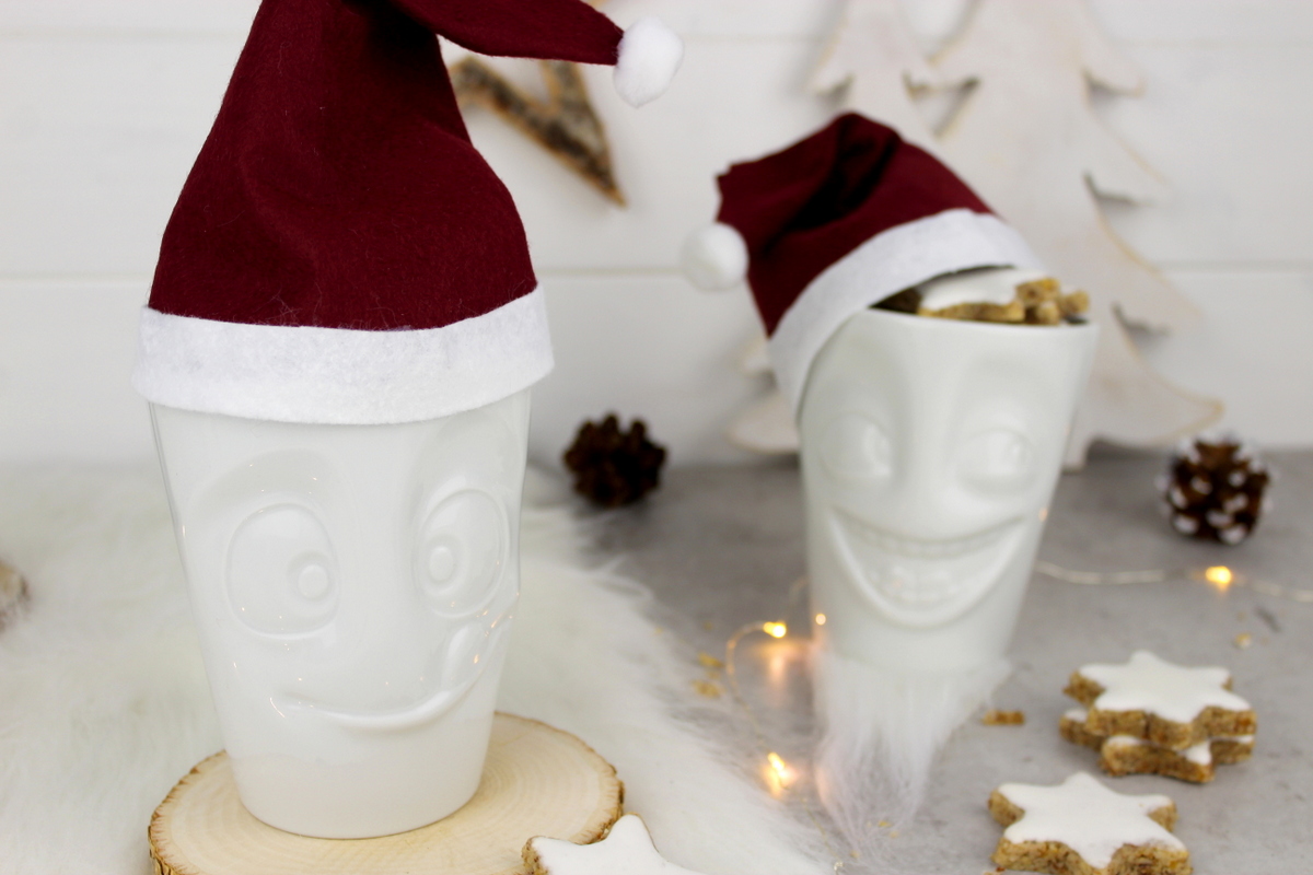 lustige Tassen mit Weihnachtsmannmützen gefüllt mit Zimtsternen