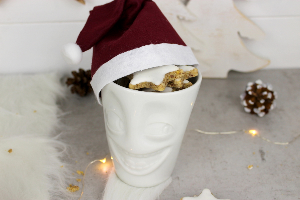 lustige Tassen mit Weihnachtsmannmützen gefüllt mit Zimtsternen