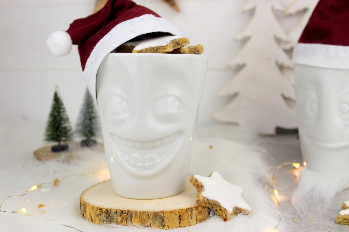 lustige Tassen mit Weihnachtsmannmützen gefüllt mit Zimtsternen